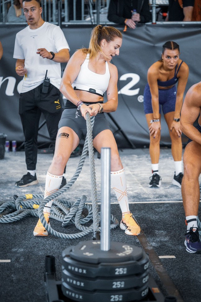 Vrouw doet een intensieve HYROX-oefening met een zwaar touw tijdens een sportwedstrijd.