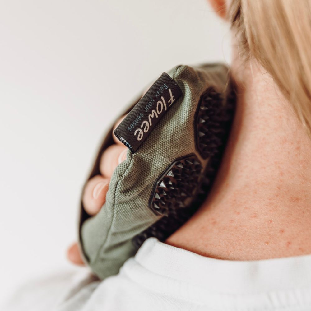 Vrouw masseert haar nek met een groene Flowee massagehand met zwarte spikes.