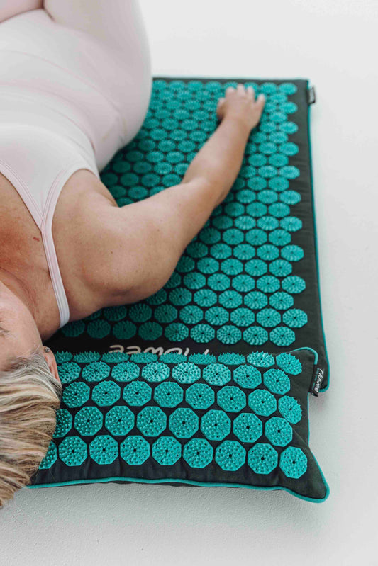 Vrouw ontspant op een grijze Flowee ECO spijkermat met zeegroene spikes en bijpassend spijkerkussen.