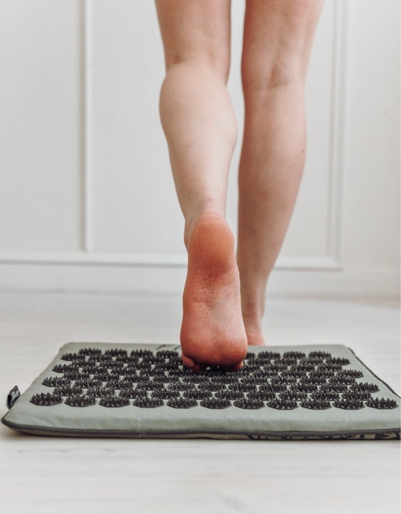 Persoon staat met blote voeten op een groene Flowee spijkermat met zwarte spikes.