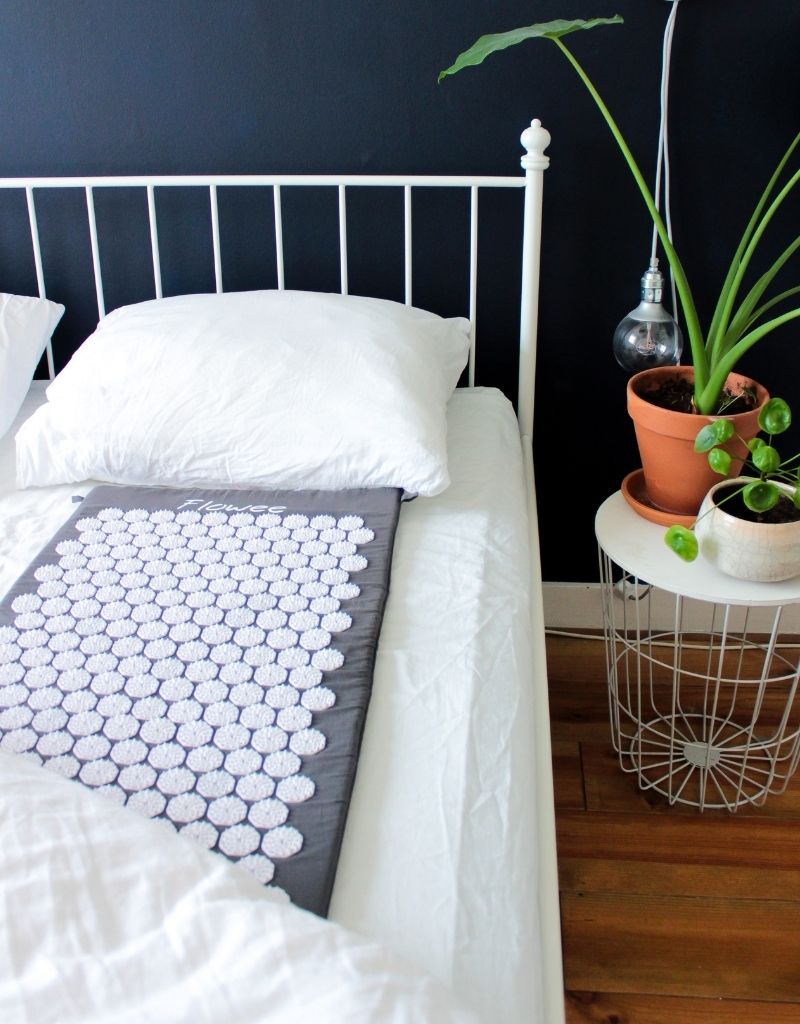 Flowee spijkermat met witte spikes ligt klaar op een opgemaakt bed.