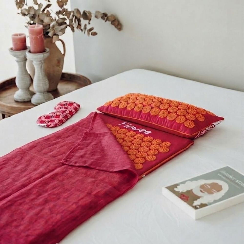Fuchsia Flowee spijkermat met oranje spikes, spijkerkussen, oogkussen en topper op bed.