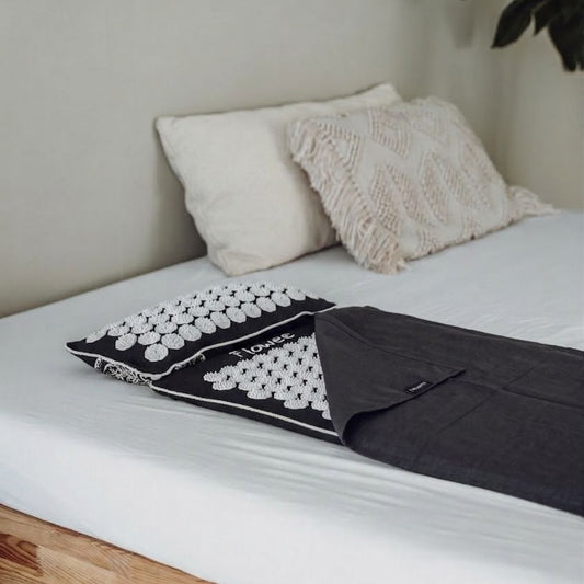 Grijze Flowee spijkermat met witte spikes, spijkerkussen en topper op bed.