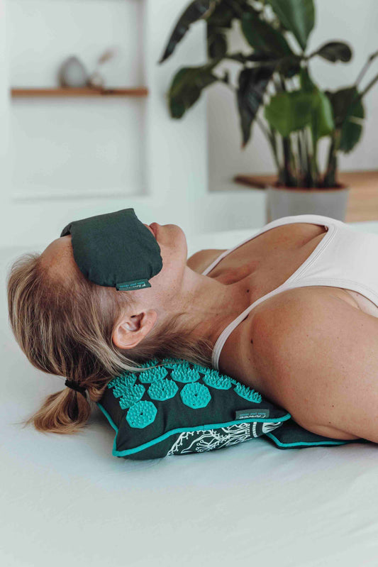 Vrouw ontspant met een Flowee Relaxset Luxe in grijs en zeegroen, met spijkerkussen en oogkussen.