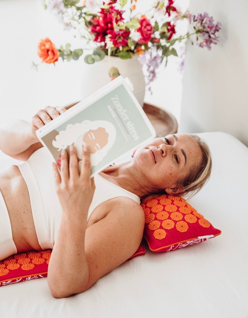 Vrouw leest ontspannen een boek op een Flowee spijkermat met spijkerkussen voor een moment zonder stress.