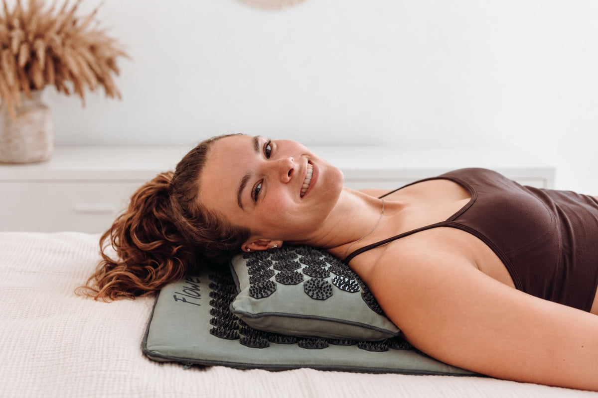 Vrouw ligt ontspannen op een Flowee spijkermat met spijkerkussen voor extra ondersteuning van nek en schouders