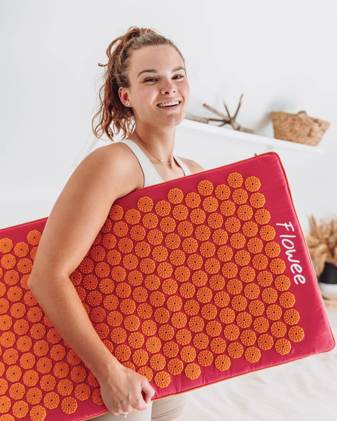 Een vrouw staat lachend met een fuchsia spijkermat met oranje spikes onder haar armen