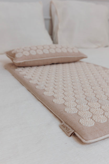Flowee Eco spijkermat set van jute in zandkleur met spijkerkussen op bed.
