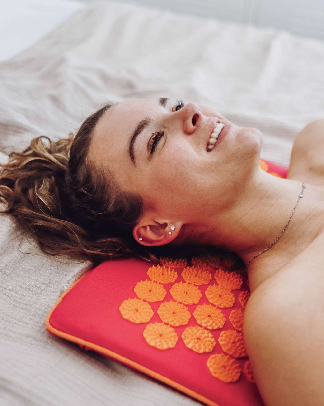 Een vrouw ligt op een bed met een spijkermat ECO in de kleur fucsia met oranje