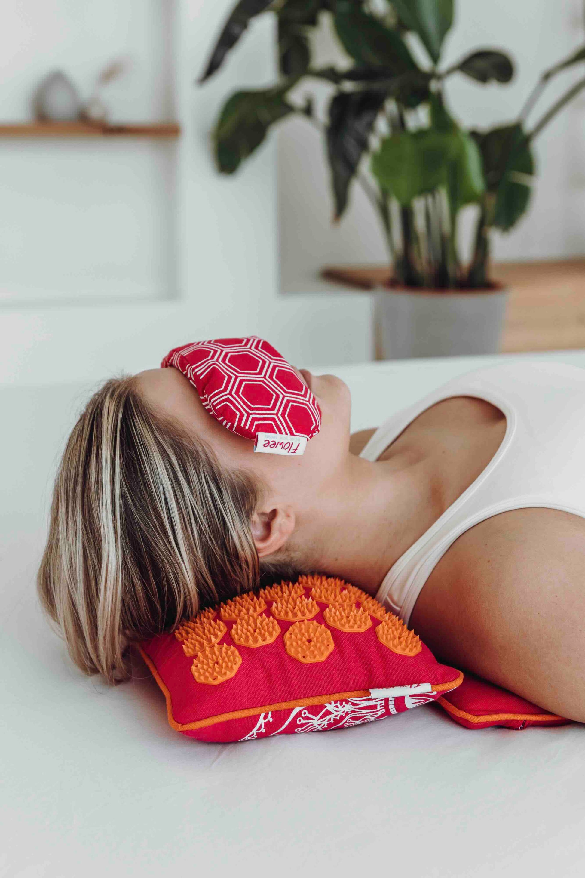 Vrouw ligt op Flowee spijkermat set in de kleur fuchsia met oranje met een oogkussen op haar ogen.