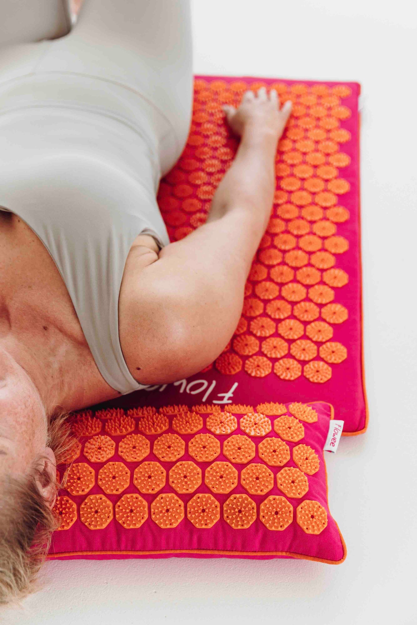 Vrouw ontspant op een fuchsia Flowee ECO spijkermat met oranje spikes en bijpassend spijkerkussen.