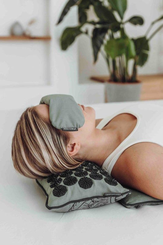 Vrouw die op flowee spijkermat ligt met haar hoofd op een spijkermat kussen. Met op haar ogen een oogkussen.