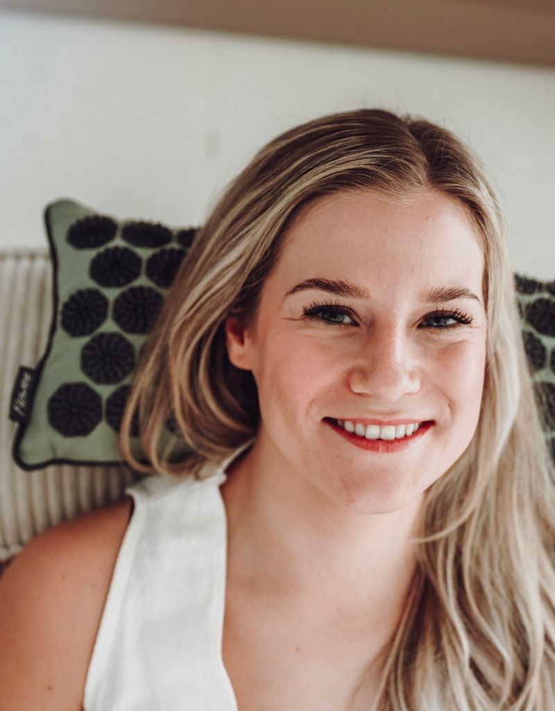 Een lachende vrouw in witte sportkleding op een relaxset luxe groen met grijs op een bed