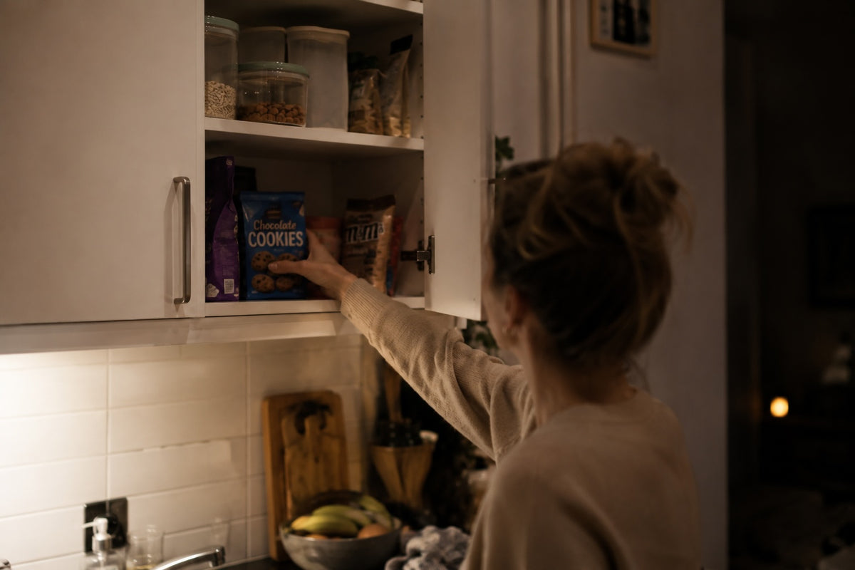 Vrouw met hongergevoel pakt koekjes uit de keukenkast tijdens het afvallen.
