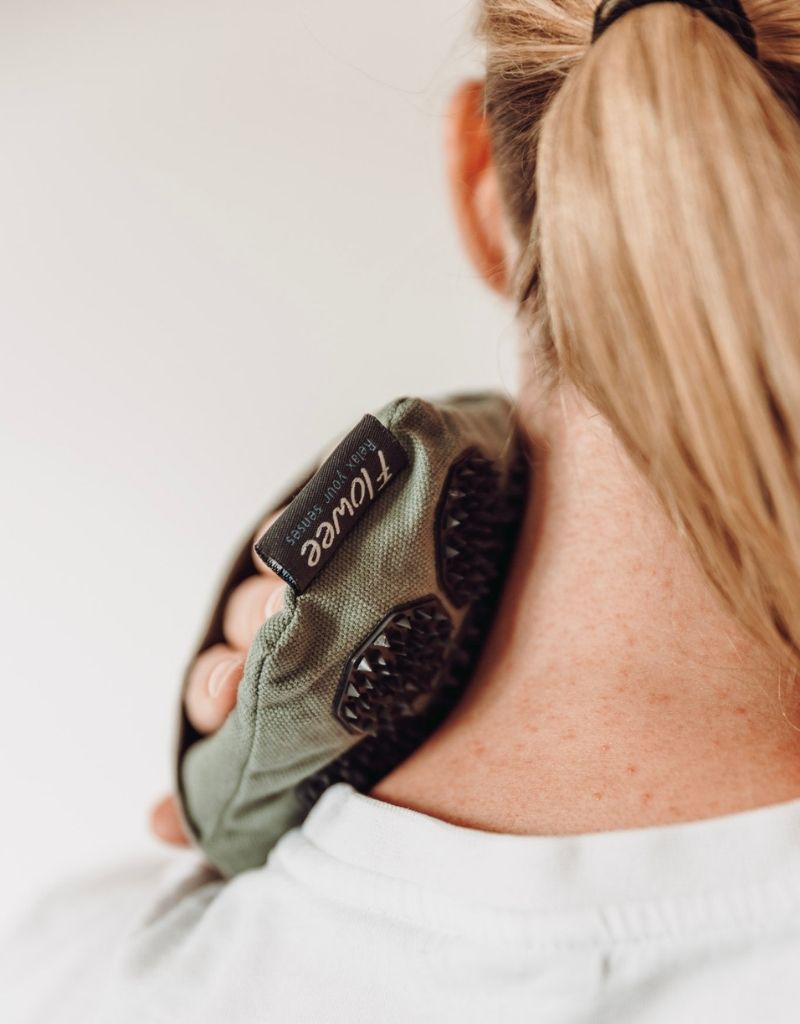 Vrouw masseert haar nek en schouders met een Flowee massagehand bij nek- en schouderklachten.