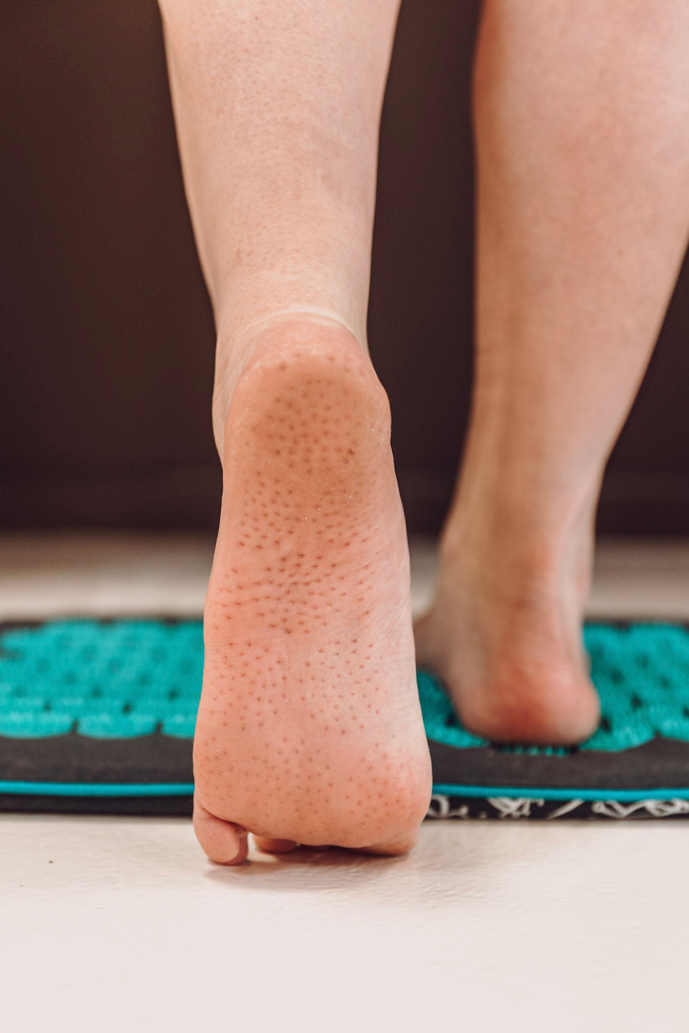 Een vrouw staat met één voet op een kleine spijkermat grijs met zeegroen, waarbij in de andere voet het resultaat van de spikes te zien is.