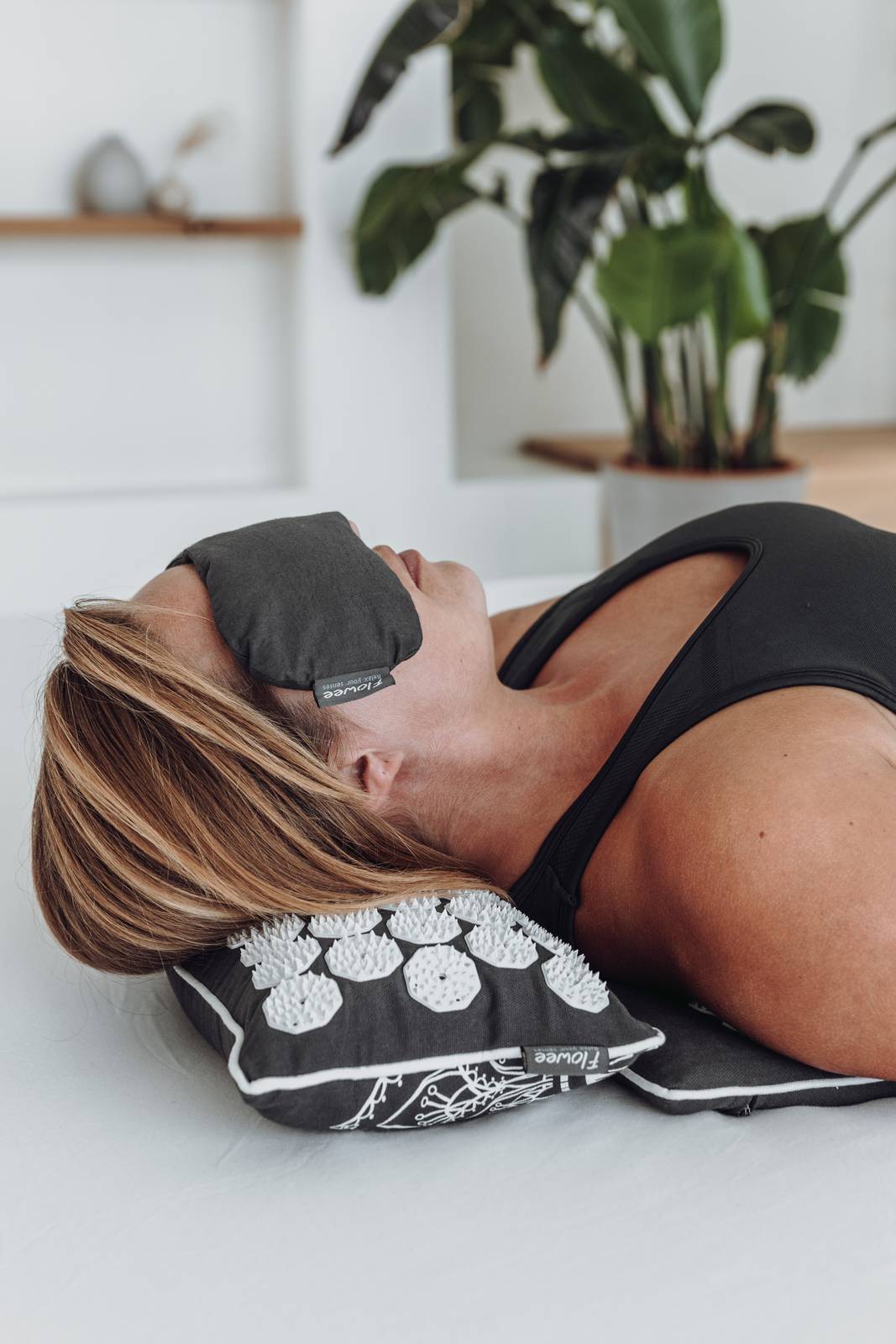 Een vrouw in zwarte sportkleding ligt op een relaxset luxe grijs met wit met een oogkussen voor haar ogen