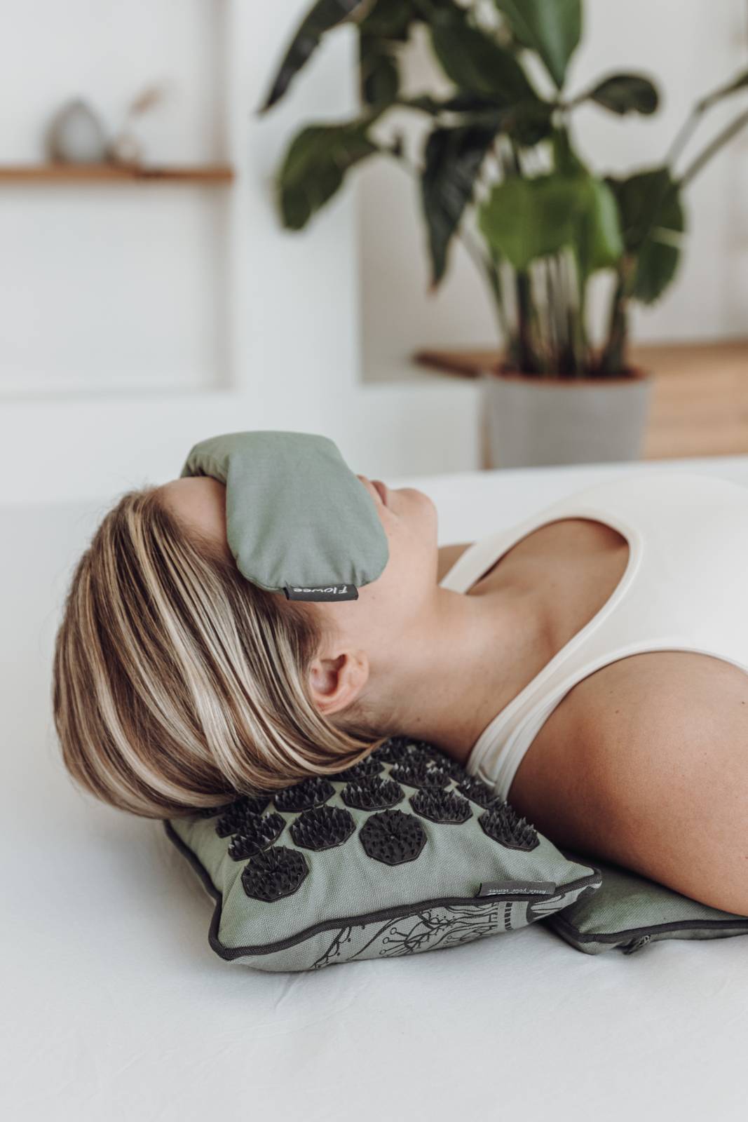 Een vrouw in witte sportkleding ligt op een relaxset luxe groen met grijs met een oogkussen voor haar ogen