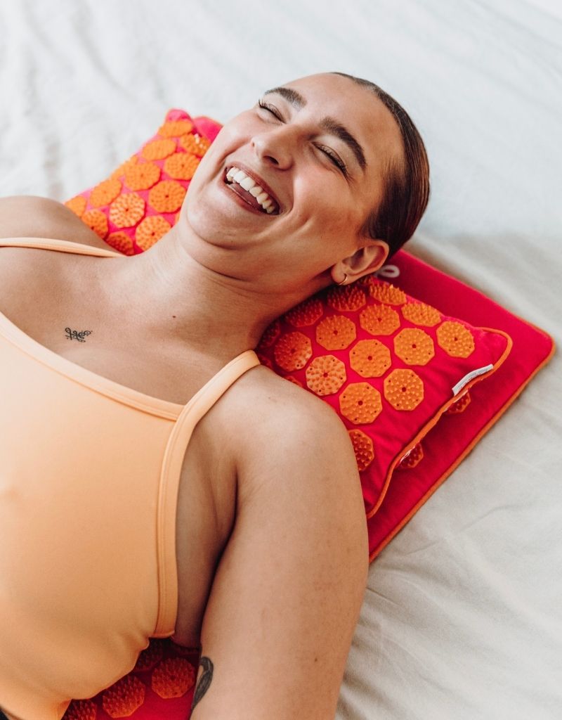 Lachende vrouw ontspant op een Flowee spijkermat met spijkerkussen voor verlichting van nek- en schouderklachten.